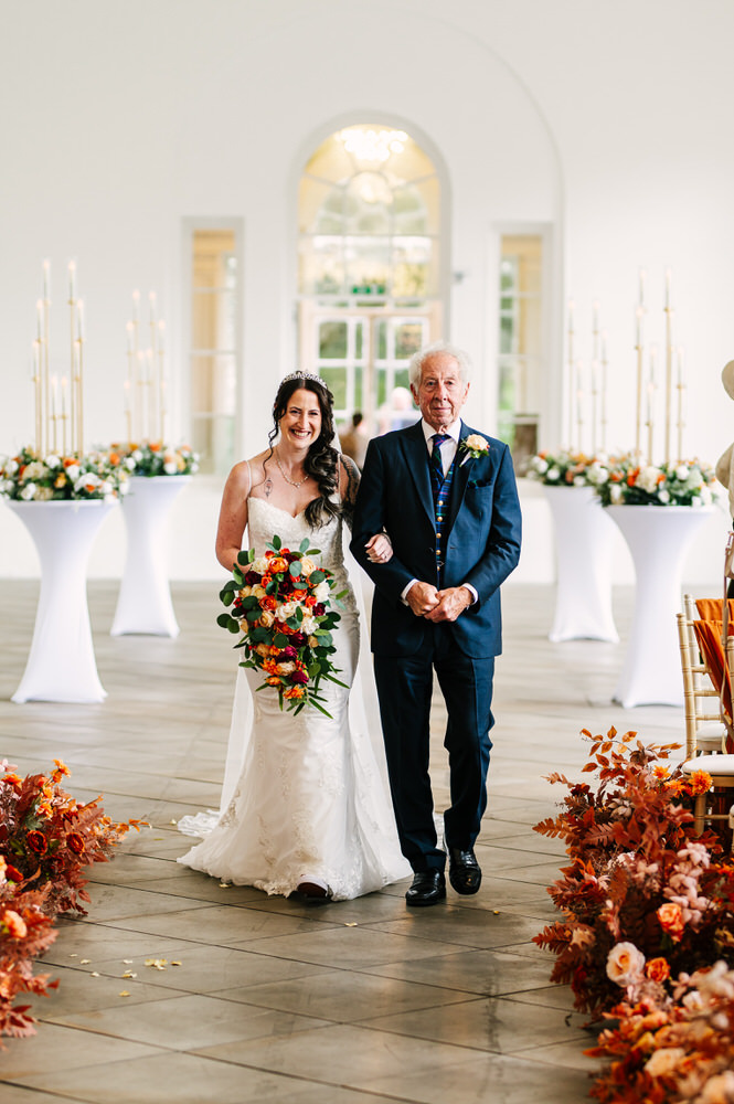 Bride walking down the isle at Margam Orangery with autumn coloured bouquet 